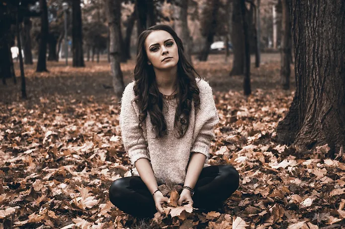 Woman sitting in a forest surrounded by autumn leaves, reflecting on mental health.