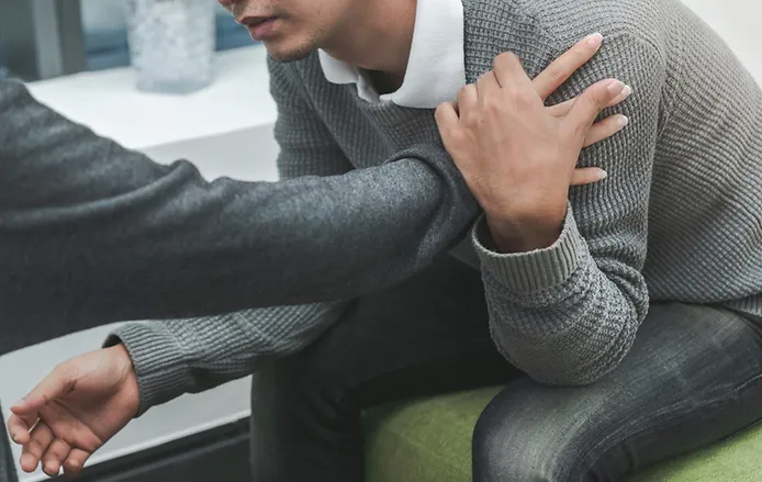 Close-up of a comforting hand on a man's shoulder during a therapy session.