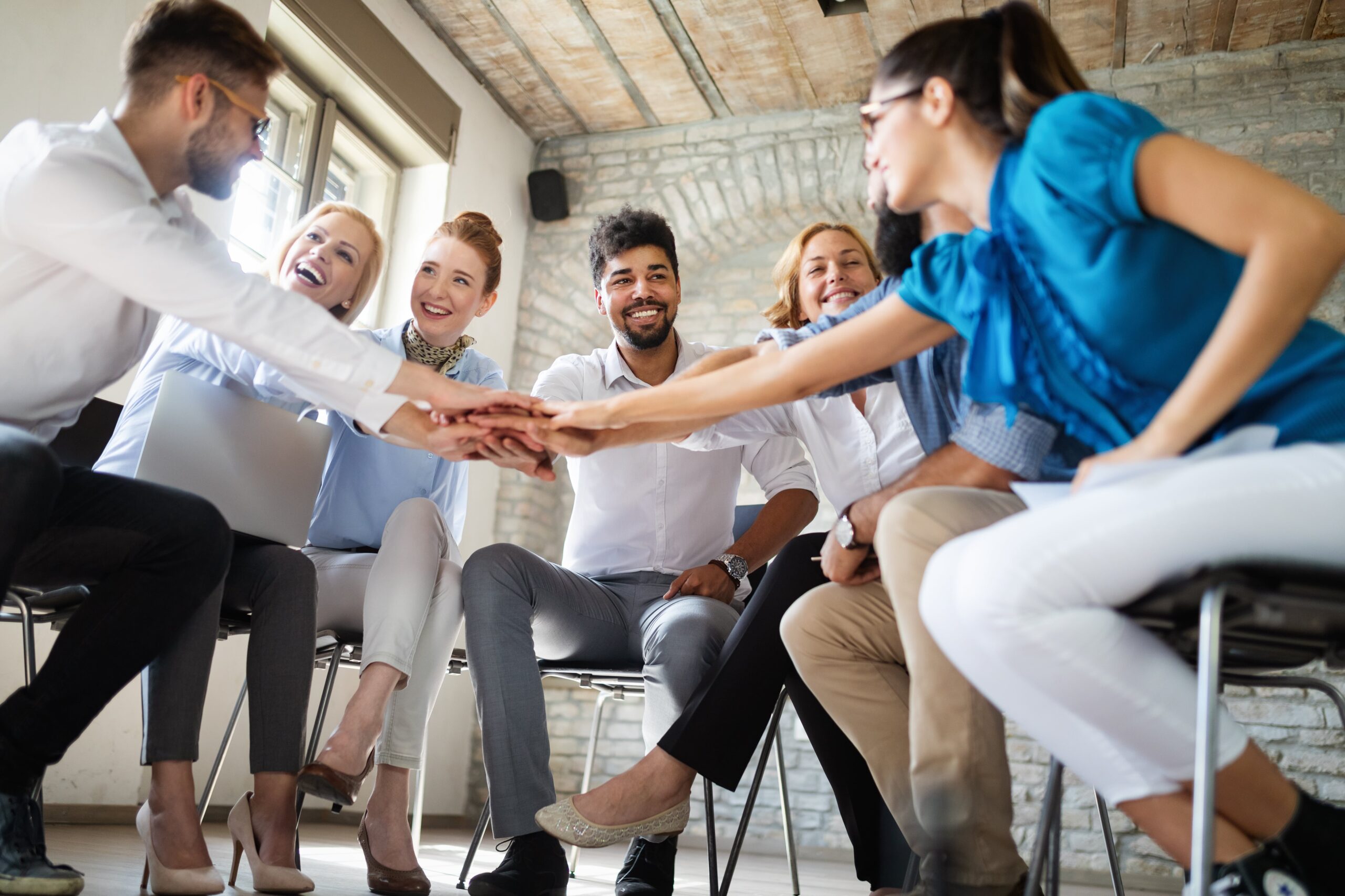 Group of diverse professionals smiling and joining hands in a show of teamwork and collaboration during a group meeting.