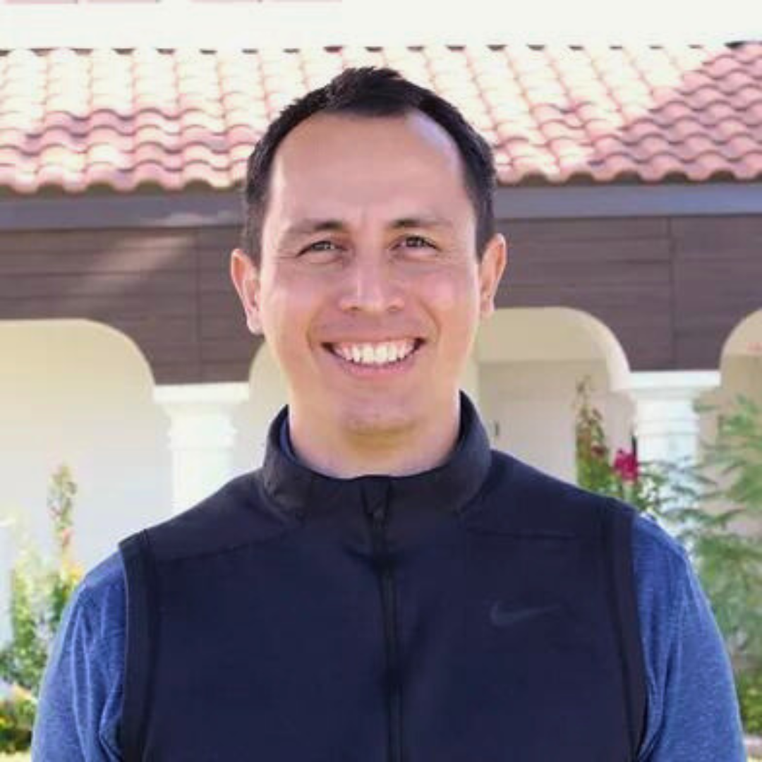 Smiling male therapist wearing a black vest, standing outside in front of a building.