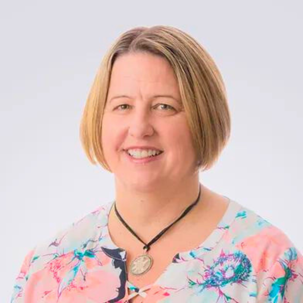 Smiling female therapist with short blonde hair wearing a floral blouse.