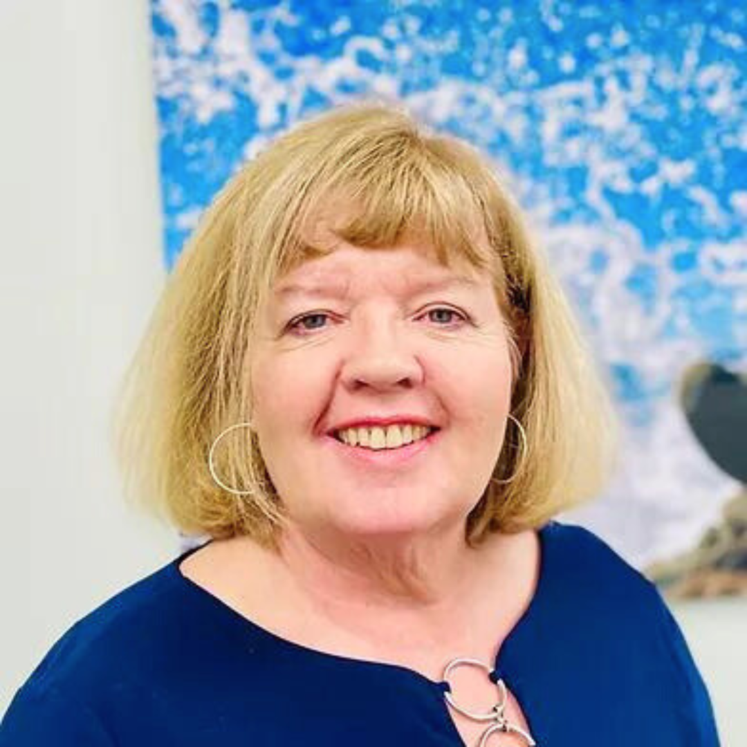 Smiling female therapist with blonde hair wearing a blue top in front of a colorful background.