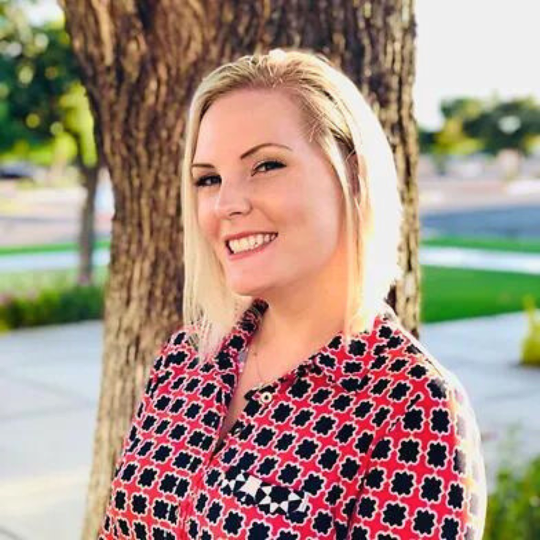 Smiling female therapist with blonde hair standing outdoors near a tree."