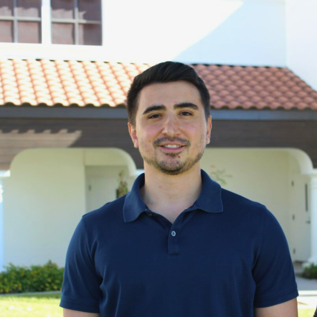 Smiling male therapist in a navy polo shirt standing outside a clinic.