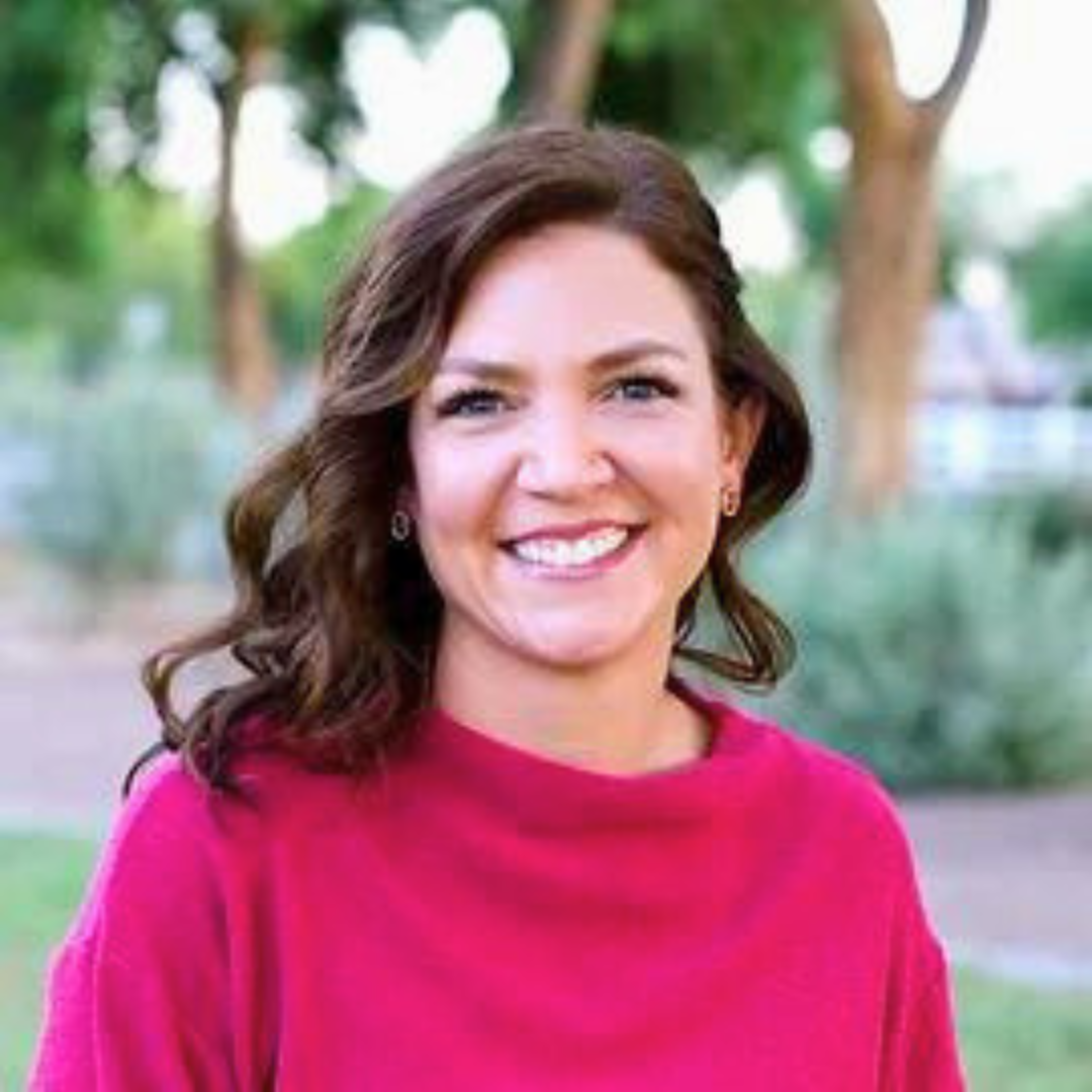 Smiling female therapist in a pink sweater standing outdoors.