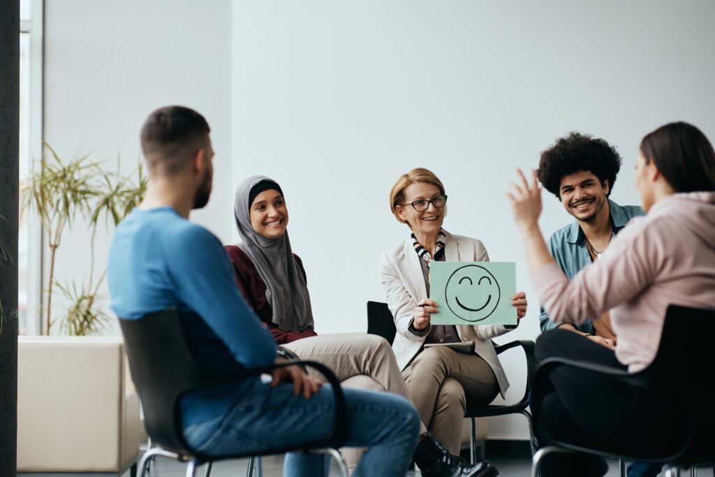 Group therapy session with a therapist holding a smiley face sign.