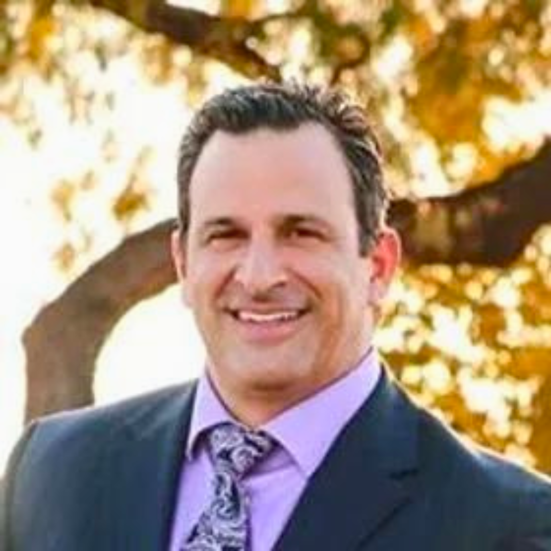 Smiling male therapist in a suit and tie standing outdoors.