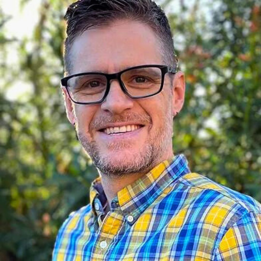 Smiling male therapist with glasses and a plaid shirt outdoors.