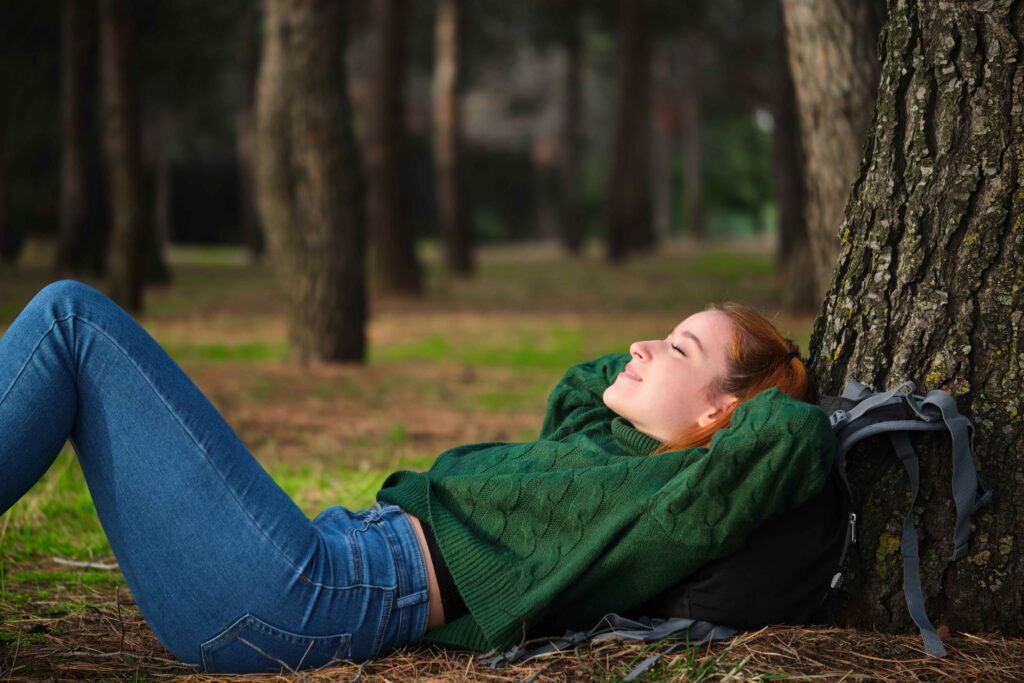 Woman relaxing against a tree in a peaceful forest, symbolizing the calming effects of mental health treatments like Spravato and TMS therapy