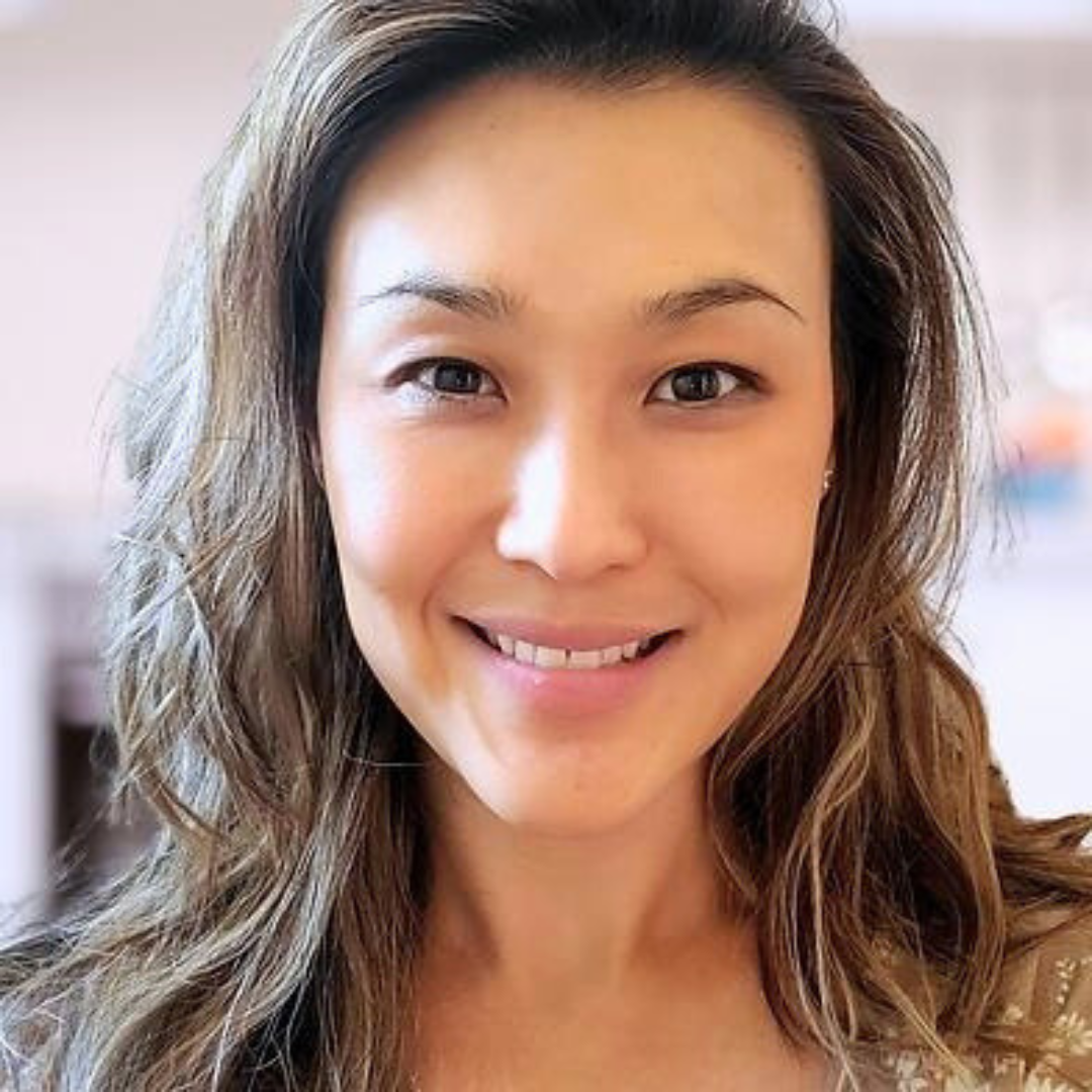 Smiling female therapist with wavy hair in a well-lit indoor setting.