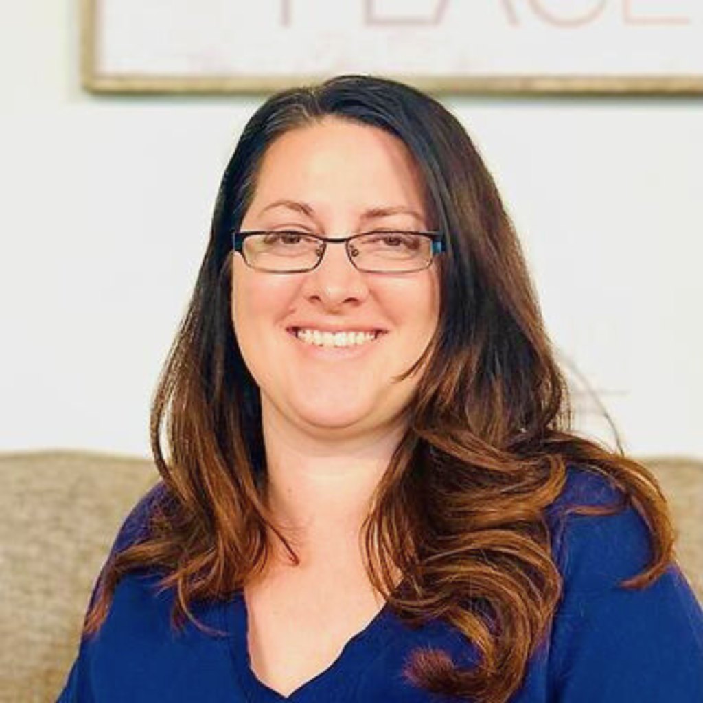 Smiling female therapist with glasses and long brown hair in a cozy setting