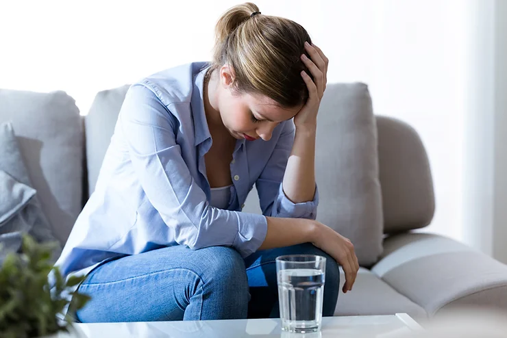 Woman sitting on a couch, holding her head in distress, symbolizing the struggles of treatment-resistant depression.