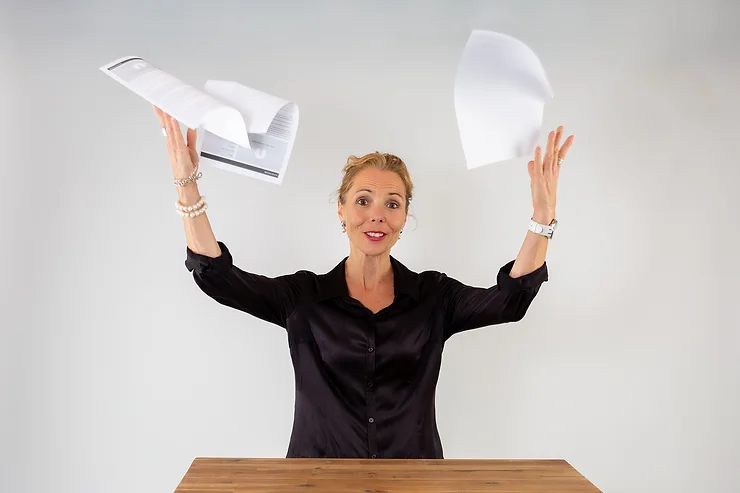 Woman joyfully tossing papers into the air, symbolizing relief from work stress.