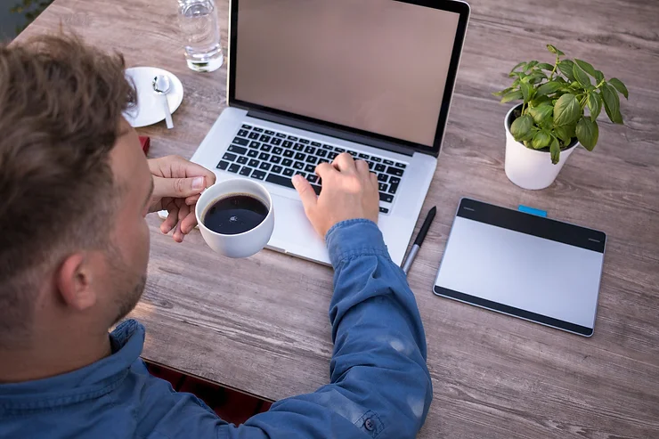 Person sitting at a desk with a laptop and coffee, symbolizing the convenience of telehealth services for mental health care.