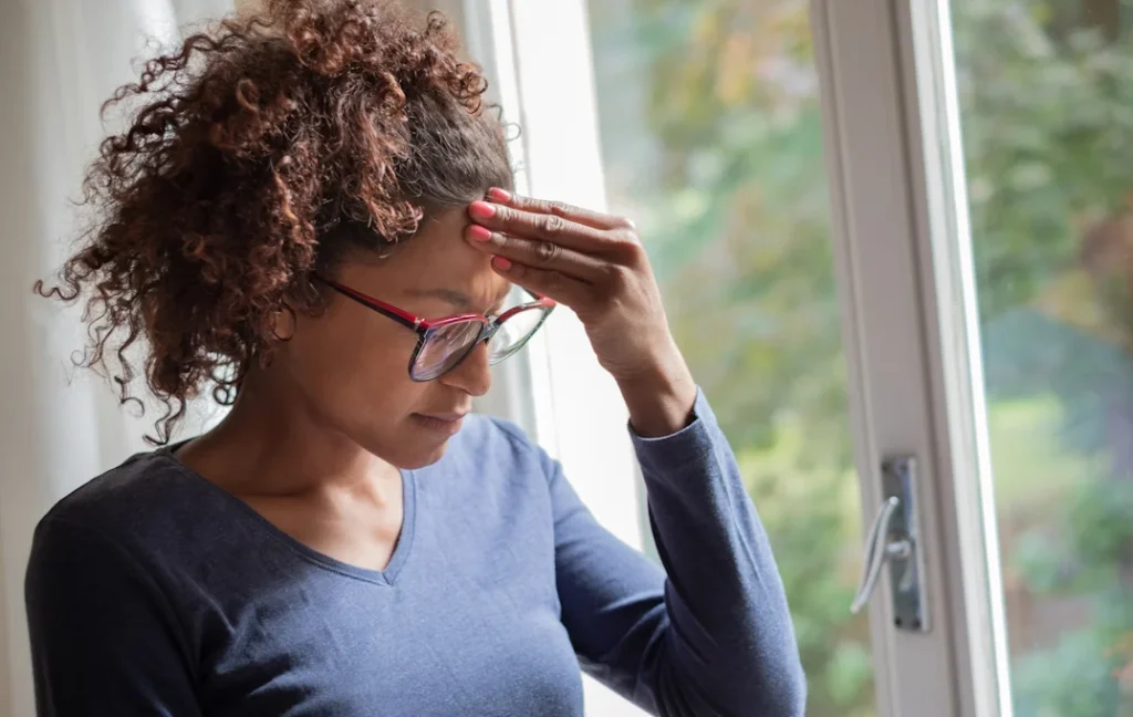 Woman standing by a window, looking thoughtful and concerned, representing the emotional barriers to seeking counseling.