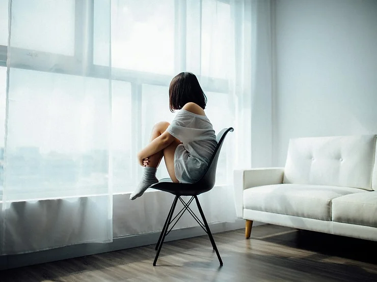 Person sitting alone on a chair by the window, reflecting on mental health and wellness.