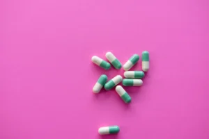 Green and white capsules scattered on a pink background.