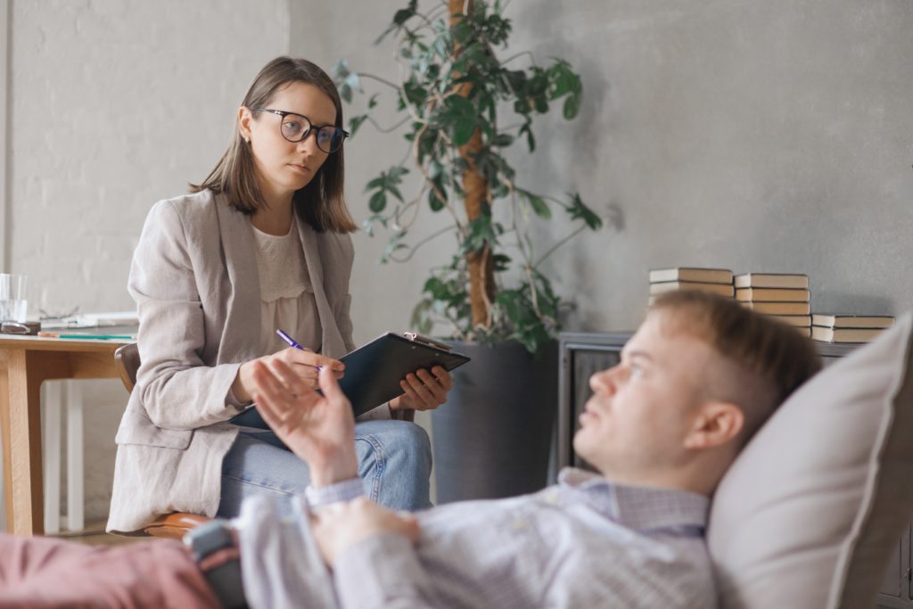 Female psychiatrist attentively listening and taking notes during a therapy session with a male patient.