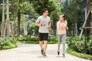 An Asian couple jogging together in a park, surrounded by greenery and enjoying a healthy lifestyle