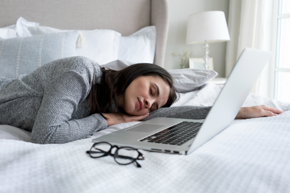 A woman peacefully sleeping on a bed beside an open laptop, creating a serene and relaxed atmosphere.