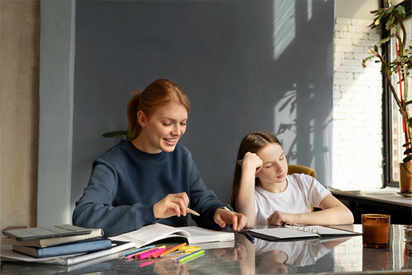 A woman and a girl are at a table, using a laptop, highlighting a shared activity and connection between them