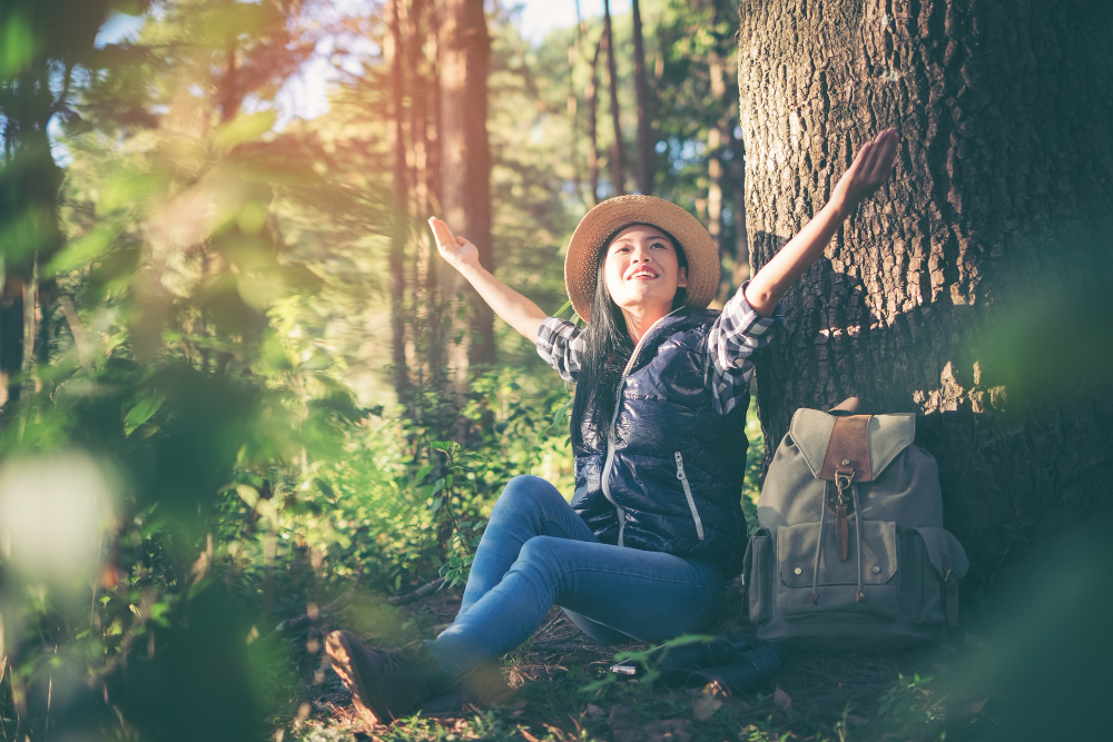 A happy woman after taking Spravato Treatment sits on the ground with her arms outstretched, expressing openness and tranquility in a serene environment.