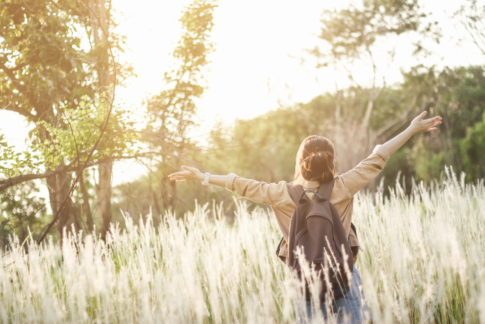 A happy woman after Ketamine Therapy stands in a field with her arms outstretched, embracing the open space and nature around her.