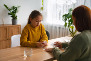 A woman and a girl are seated together at a table, engaged in conversation and sharing a moment of connection