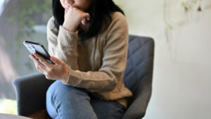 A woman seated on a chair, engaged with her phone, displaying a relaxed and focused demeanor