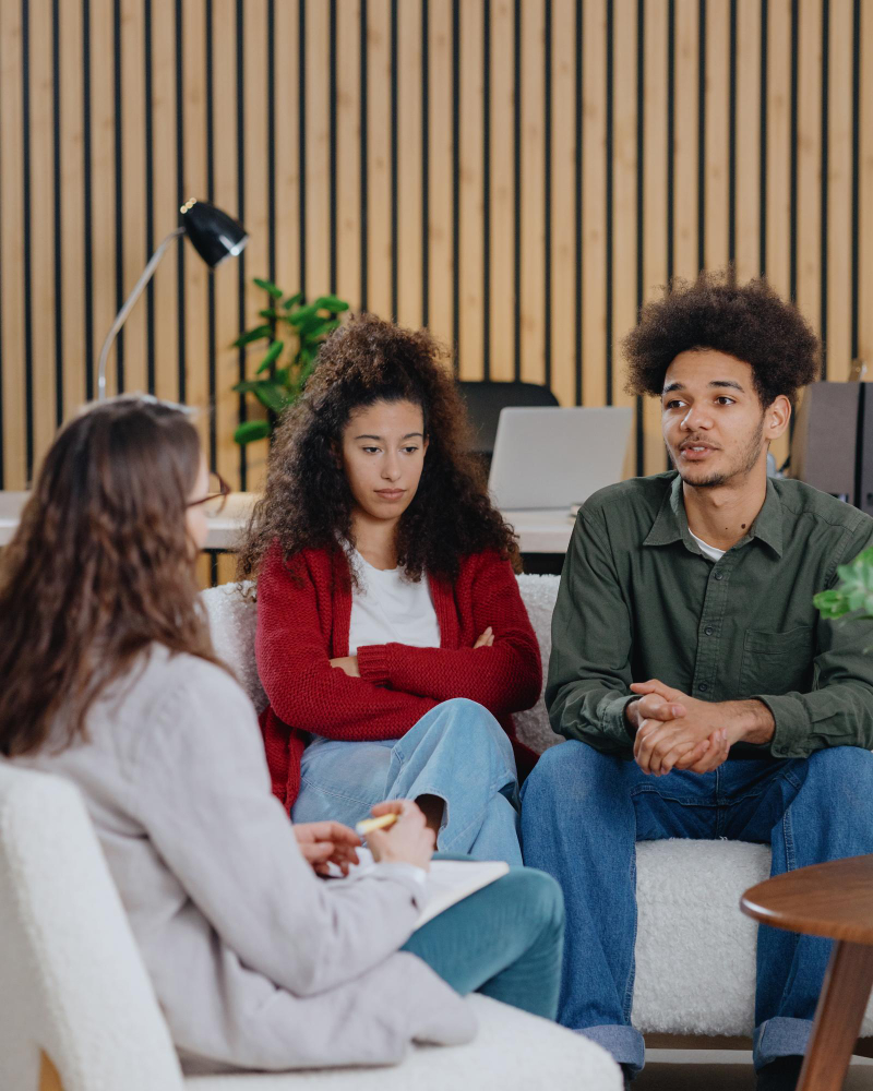 Three individuals engaged in a group therapy with a psychiatrist while seated on a comfortable couch in a cozy setting