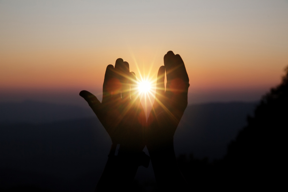 Hands reaching skyward, illuminated by sunlight, symbolizing hope and aspiration.