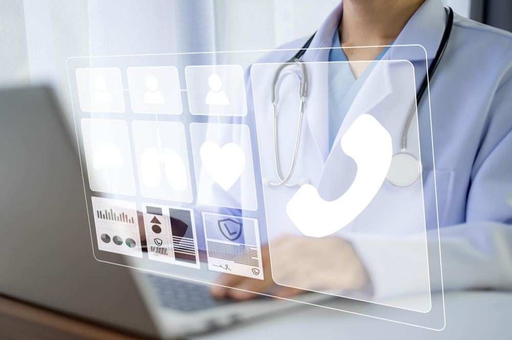 A physician using a laptop, with a mobile phone resting on it, engaged in a task in a medical environment