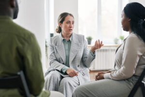 A woman speaks to two colleagues during a meeting, engaging in discussion and sharing ideas