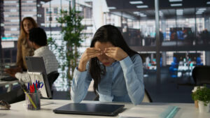 A woman struggling with anxiety sits at a desk, resting her face in her hands, appearing deep in thought or contemplation