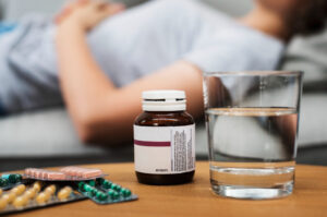 Woman sleeping on a couch beside psychiatric medication and a glass of water, indicating a moment of rest or recovery