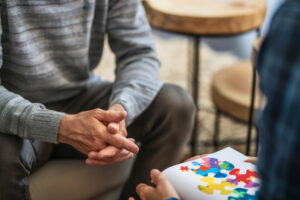 A man sitting on a couch holds a puzzle piece, undergoing Cognitive Behavioral Therapy.