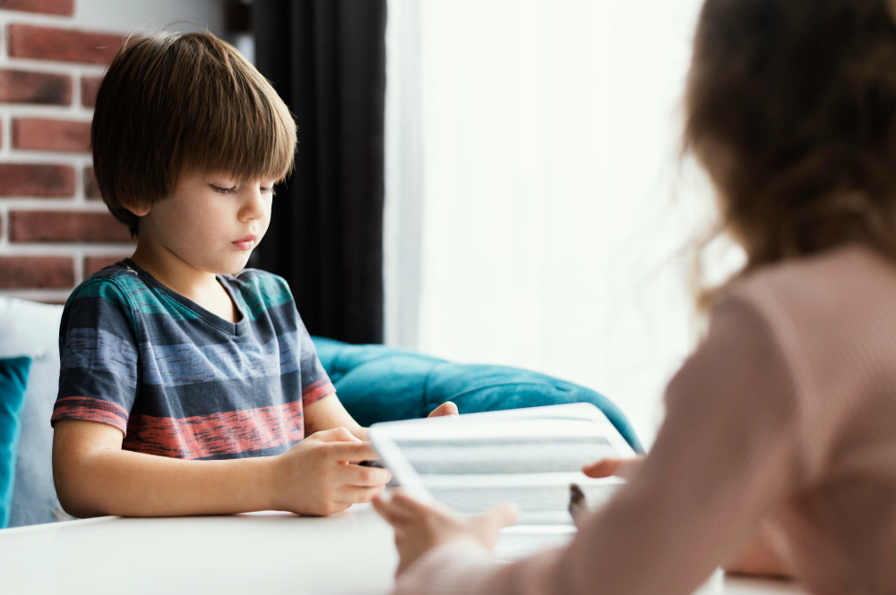 A young boy sitting at a table, focused on using a tablet in front of him. Psychiatric Therapy for Children and Adolescents: A Parent’s Friendly Guide.