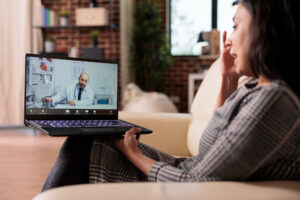 A woman sitting on a couch, engaged in a Telepsychiatry video call on her laptop