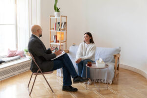 A man and woman sitting together on a couch in a cozy room, engaged in a mental health therapy.