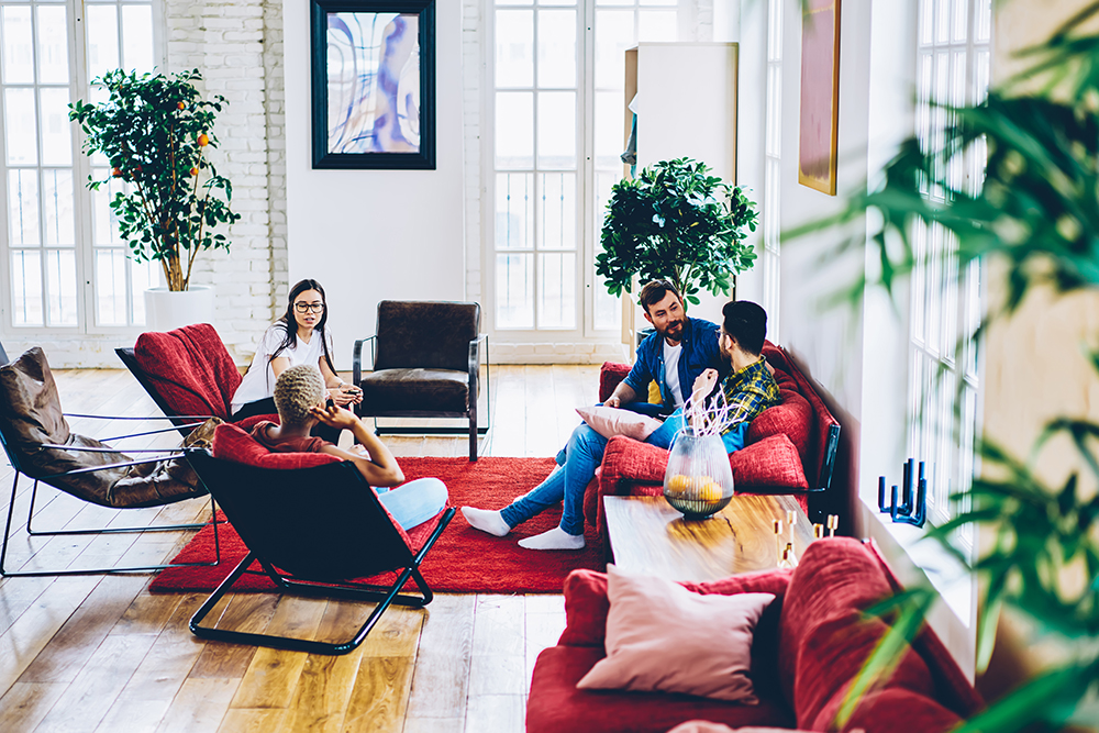 Young male and female best friends resting in modern designed apartment communicating about comfort, diverse woman and man 20s have homey conversation on leisure in stylish hostel living room